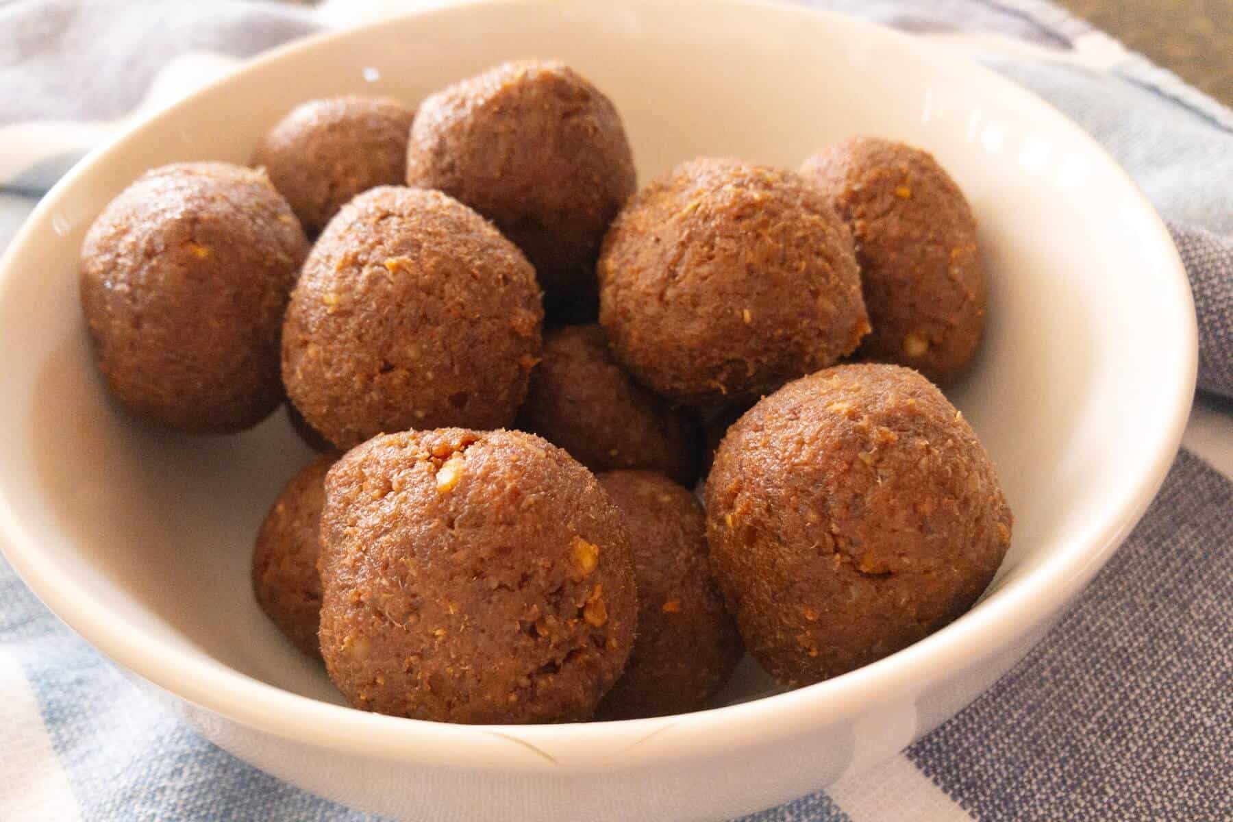 White bowl of brown quinoa date balls sitting on a table.