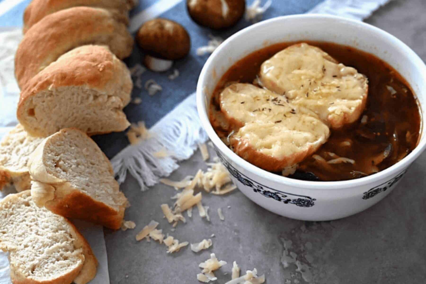 A loaf of French bread next to a bowl of vegetarian French onion soup.